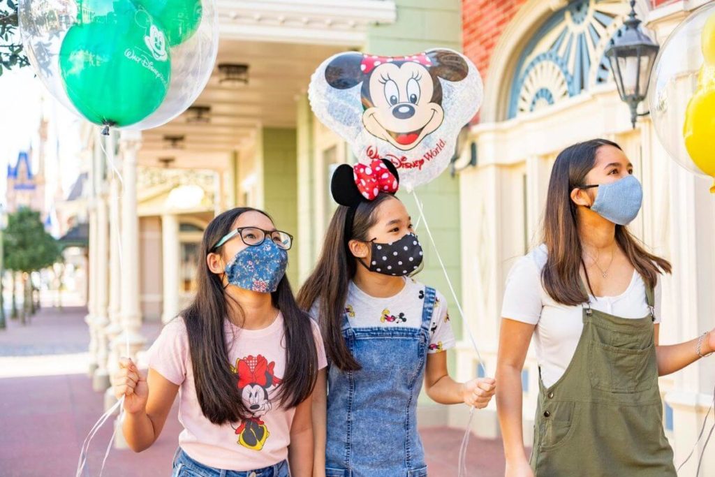  Bilde av en kvinne og 2 barn iført beskyttende ansiktsmasker mens På Disney World.