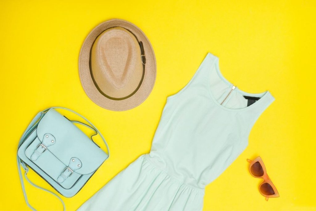  Foto plana de un bolso de menta, sombrero de paja, gafas de sol de coral y un vestido sin mangas de jersey de menta.
