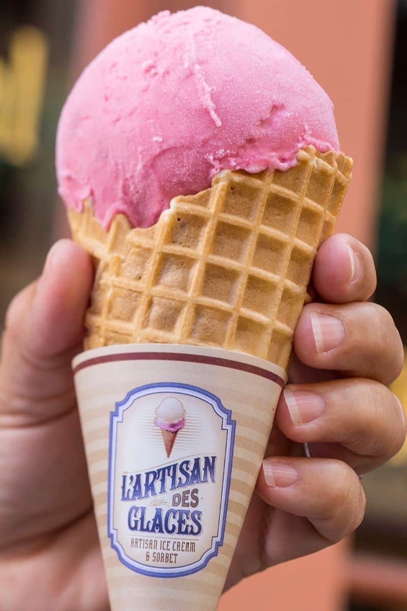 Closeup of a person holding a waffle cone filled with a scoop of pink ice cream.