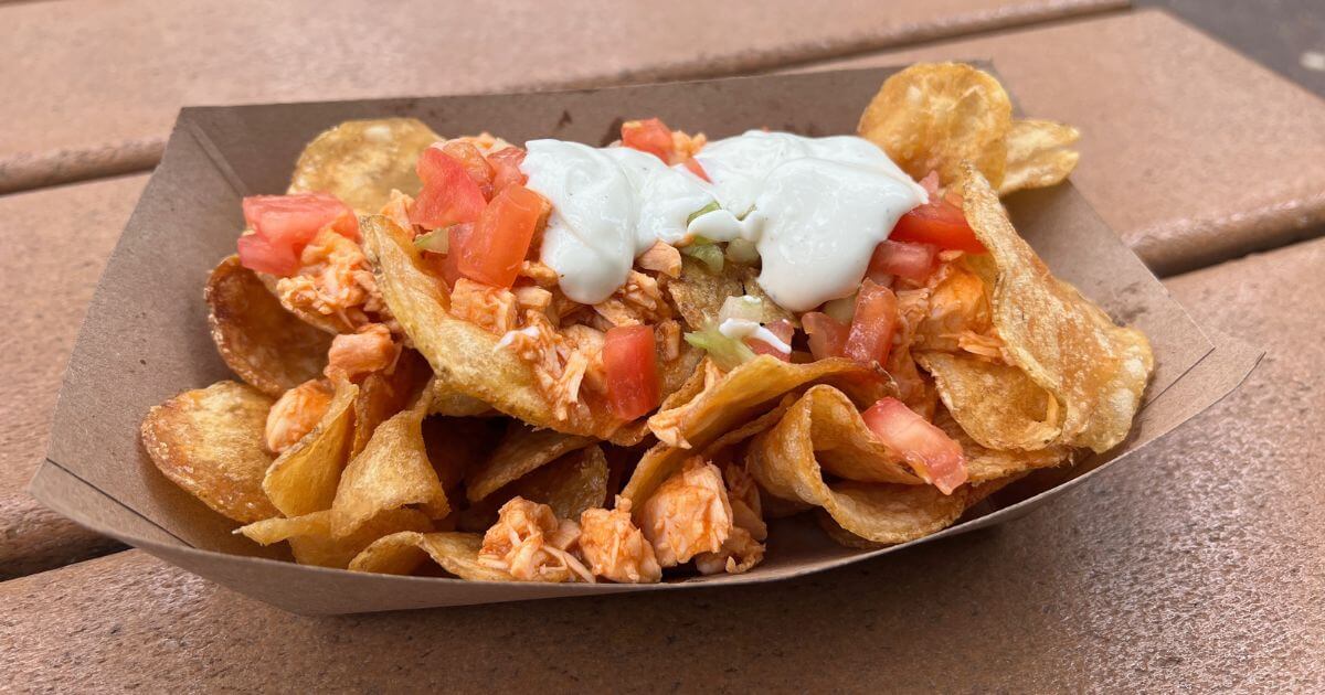 Horizontal photo of homemade potato chips topped with buffalo chicken, celery, tomato, and bleu cheese dressing.