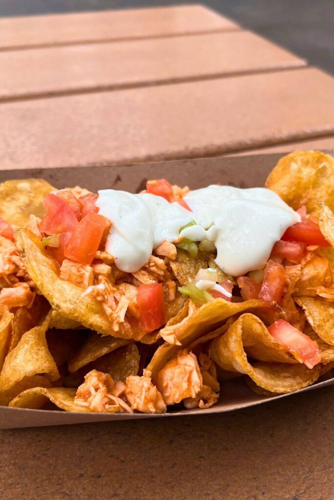 Vertical photo of homemade potato chips topped with buffalo chicken, celery, tomato, and bleu cheese dressing.