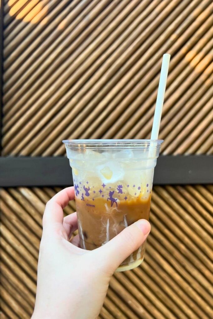 Photo of a coconut flavored cold brew coffee with a sweetened condensed milk drizzle, held against a textured wall.