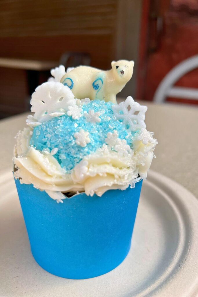 Photo of a gingerbread cupcake in a blue wrapper with blue and white frosting, snowflake candies, and a white chocolate polar bear on top.