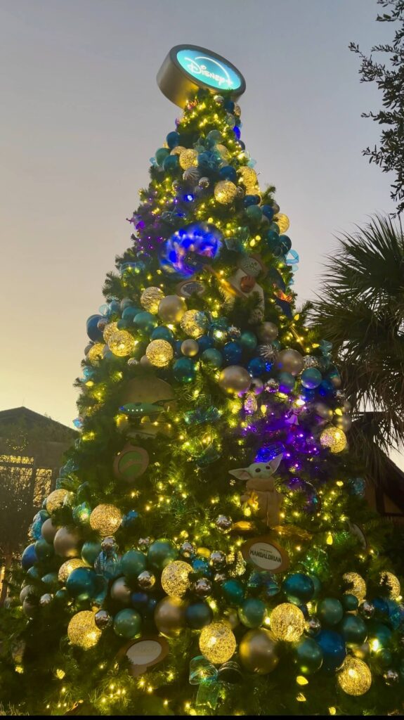 Photo of the 2024 Disney Plus themed tree at Disney Springs at night with the lights on.