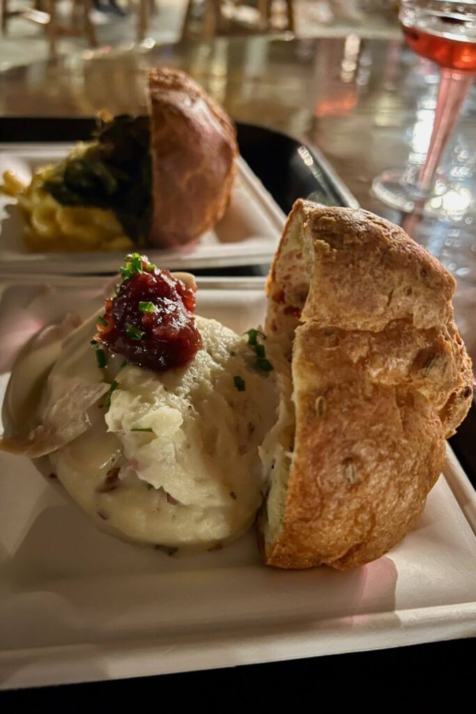 Photo of holiday dinner themed popovers, including one with turkey and cranberry sauce and another with mac-n-cheese and collard greens. In the background is a cranberry cocktail.